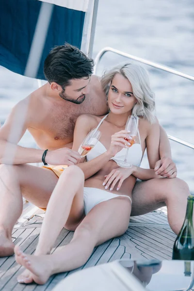 年轻的微笑夫妇在泳装放松与香槟眼镜在游艇上 — 图库照片