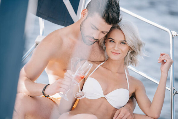 young couple in swimwear clinking by champagne glasses on yacht 