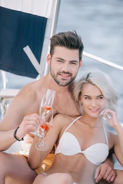 微笑的年轻夫妇在泳装放松与香槟眼镜在游艇上 — 图库照片
