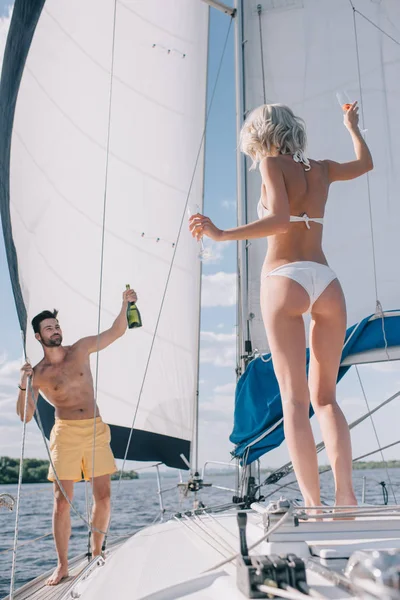 英俊的无上衣男子展示瓶香槟给女朋友戴眼镜在游艇上 — 图库照片