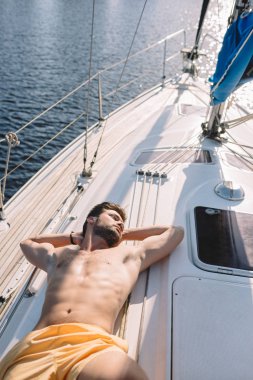 high angle view of shirtless muscular man in swim trunks having sunbath on yacht  clipart