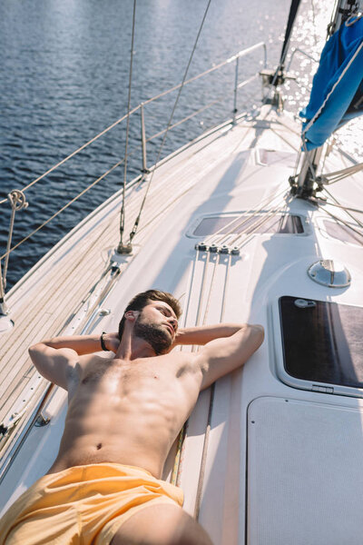 high angle view of shirtless muscular man in swim trunks having sunbath on yacht 