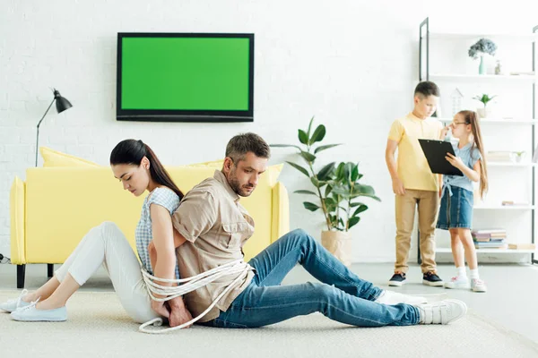 親概念床と自宅でクリップボードを保持している子供たちにロープで縛られて座っている親は — ストック写真