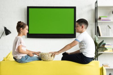 side view of sister and brother eating popcorn at home clipart