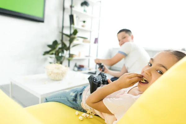 姐姐和哥哥在家里玩电子游戏和吃爆米花 — 图库照片