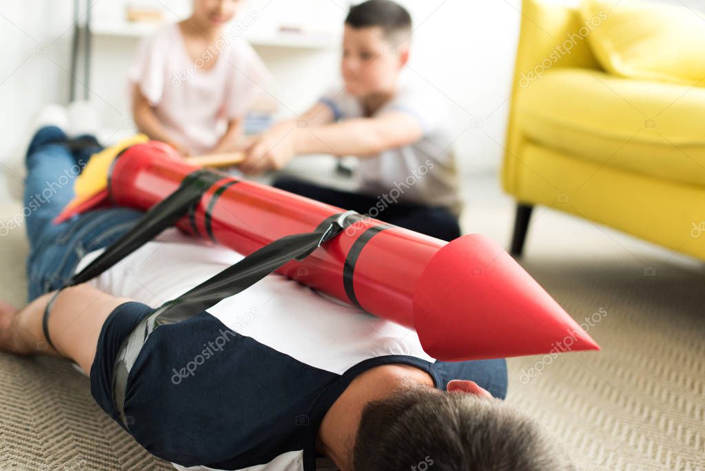 tied father with rocket toy lying on floor and children playing with him, parenthood concept