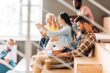 genç öğrenci tribün arkadaşlarıyla otururken dizüstü kullanarak yan görünüm