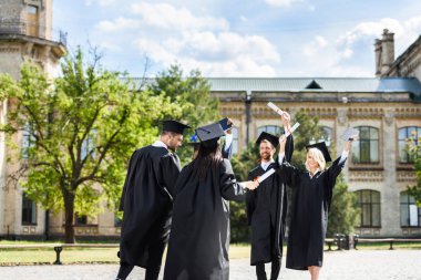 Genç mezun öğrencilerin üniversite bahçesinde birbirlerini tebrik diploma ile
