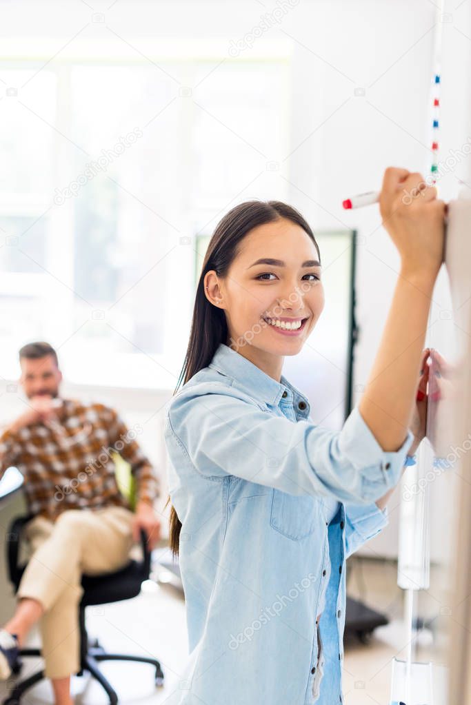 happy asian student girl writing on whiteboard during lesson with blurred teacher on background