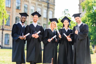 Genç mezun öğrencilerin diploma tutarak ve kameraya bakarak burun içinde