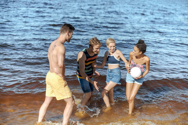 happy interracial group of friends with volleyball ball having fun by sea