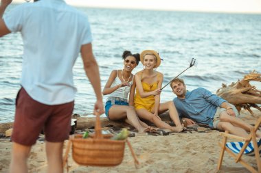piknik sepeti ve çok ırklı arkadaş olan adam kısmi görünümü kum plajındaki