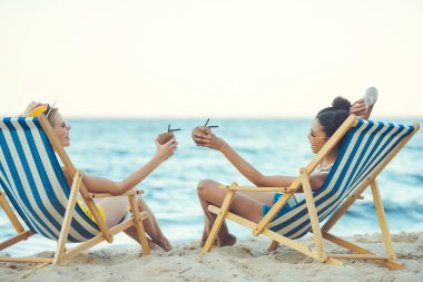 plaj sandalyeleri deniz tarafından dinlenme Hindistan cevizi kokteyller ile genç çok ırklı kadınlar