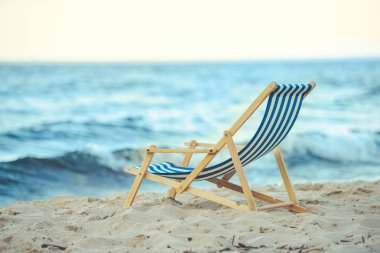 selective focus of wooden beach chair on sandy beach with sea on background