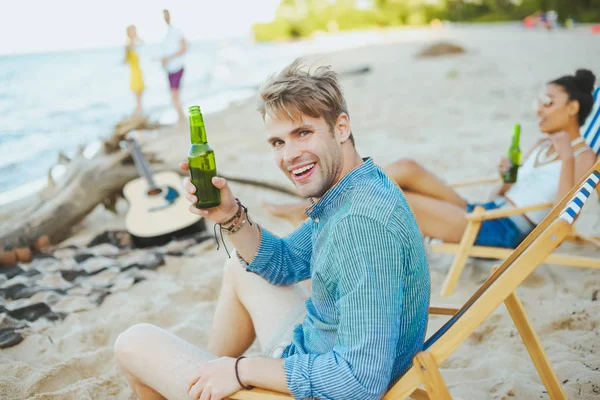 selective focus of group of friends with beer resting on sandy beach together