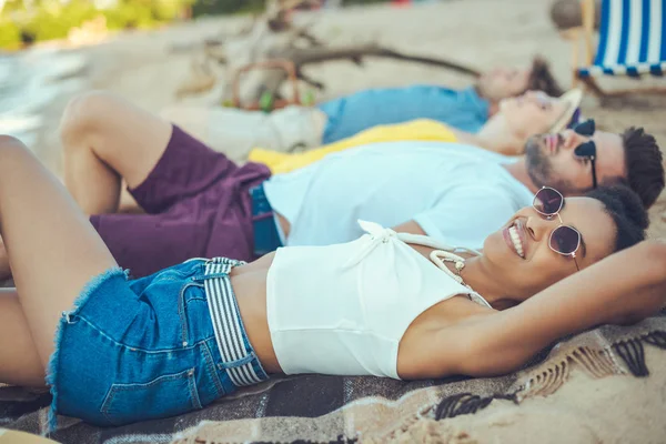 砂浜のビーチでの時間を過ごしながら毛布の上に横たわる多民族の若者たちの選択と集中 — ストック写真
