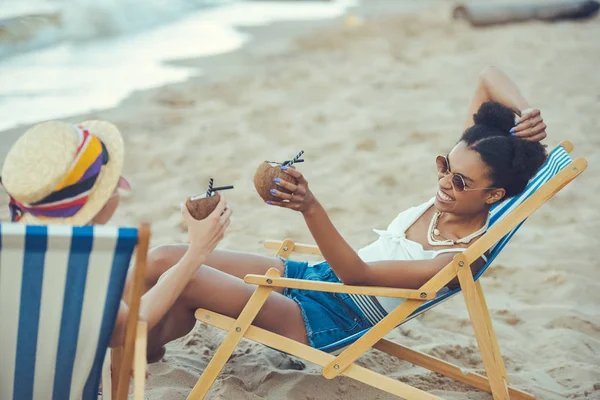 Молоді Багатоетнічні Жінки Кокосовими Коктейлями Відпочивають Пляжних Стільцях Біля Моря — стокове фото