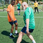 Selektiv fokus för mångkulturella äldre vänner spelar fotboll tillsammans