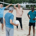 Multicultural old friends playing volleyball on beach on summer day
