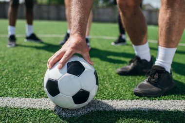 partial view of old player holding football ball with multiracial friends behind on football field clipart