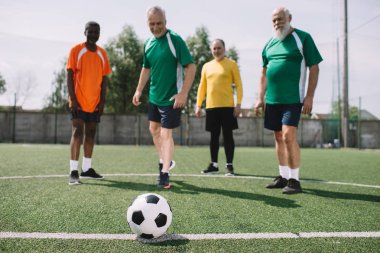 futbol topu ve çok kültürlü yaşlı erkekler yeşil futbol sahası üzerinde seçici odak