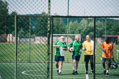 sportif su şişeleri futbol sahasında yürüyüş ile Interracial yaşlı sporcu grubu