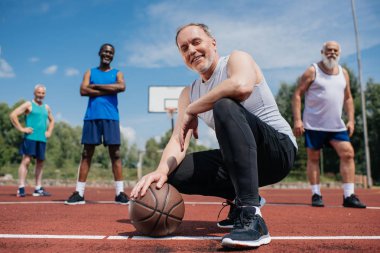 selective focus of multiethnic elderly sportsmen with basketball ball on playground clipart