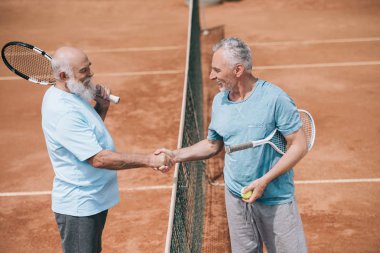 oyun sahasında sonra el sıkışan tenis raketleri ile yaşlı arkadaş gülümseyen yan görünümü