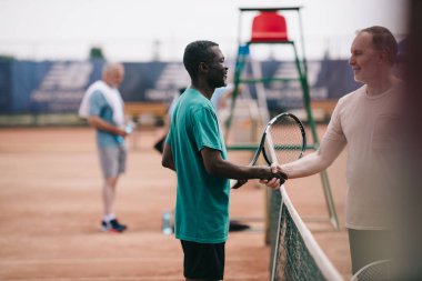 oyun sahasında sonra el sıkışan tenis raketleri ile Interracial yaşlı arkadaş seçici odak