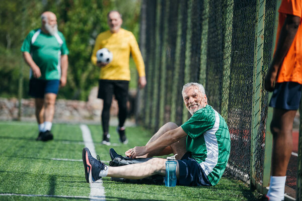 selective focus of interracial elderly football players after match on green field