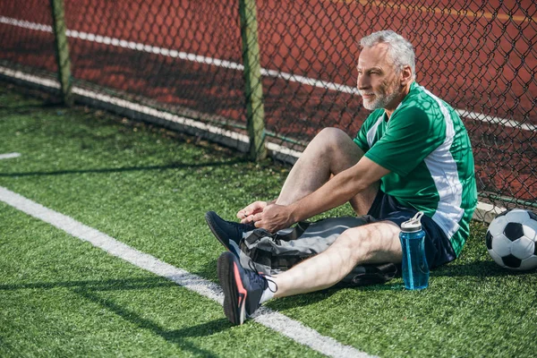 side view of old man tying shoelaces on football field