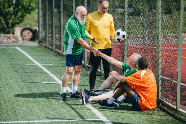 緑のフィールドで試合後に握手の異人種間の高齢者のサッカー選手 — ストック写真