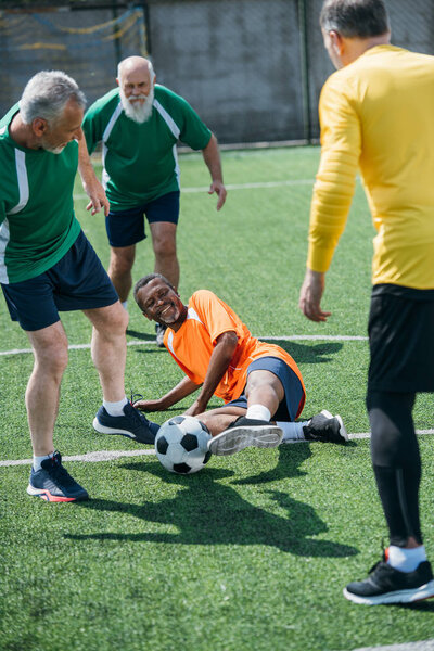 smiling multicultural elderly friends playing football together