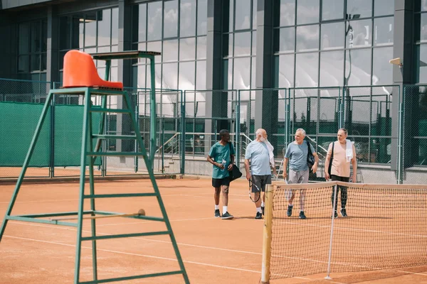 Çok Irklı Yaşlı Arkadaş Sahada Yürüyüş Tenis Malzemeleri Grubu — Stok fotoğraf