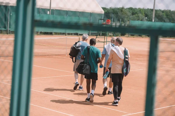 Rückansicht Von Multirassischen Älteren Freunden Mit Tennisausrüstung Beim Gehen Auf — Stockfoto