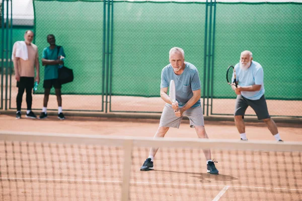 selective focus of old sportsmen playing tennis on court