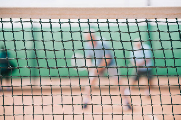 selective focus of net on court and players with tennis equipment
