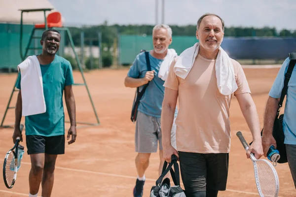 多种族老年朋友在球场上行走网球器材的选择性聚焦 — 图库照片