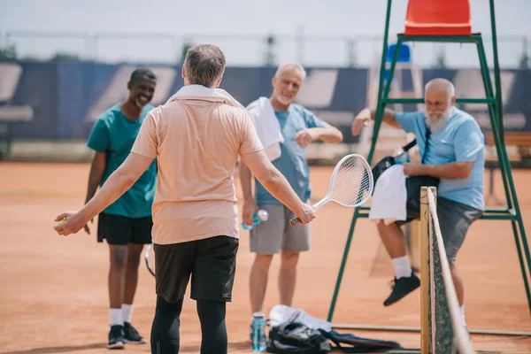 selective focus of old multiethnic friends on tennis court on summer day