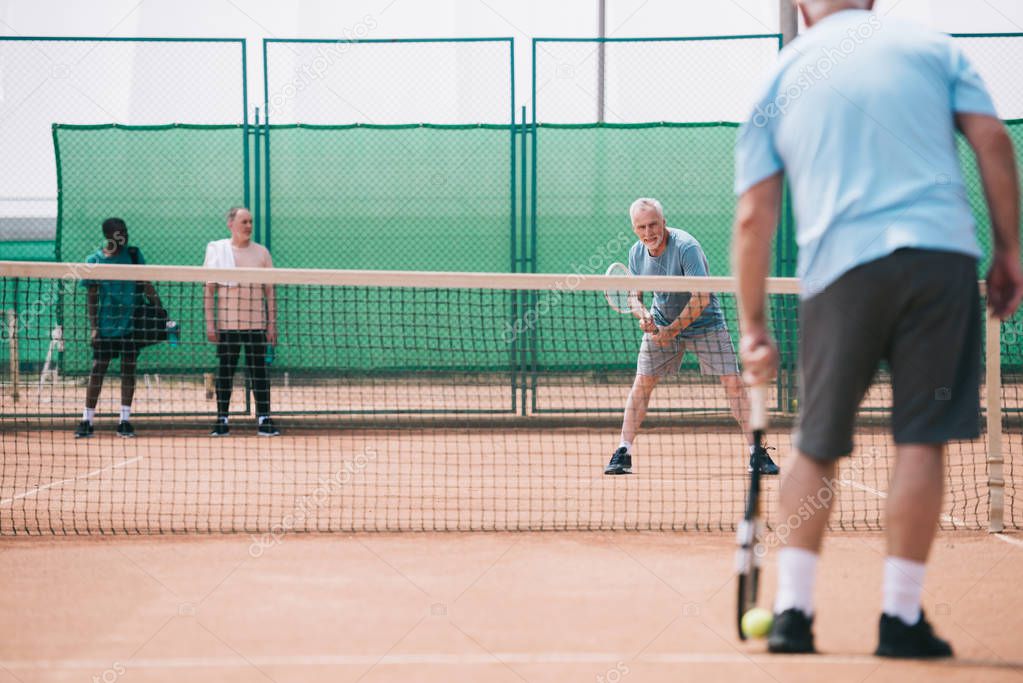 selective focus of old sportsmen playing tennis on court