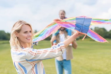 happy family with one child playing with colorful kite in park clipart