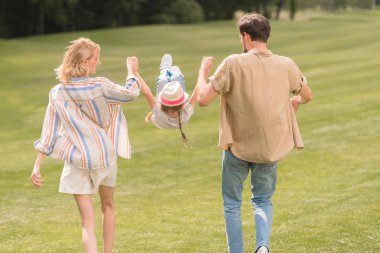arkadan görünüşü ailesi ile el ele tutuşarak ve having fun birlikte parkta yürürken küçük kızı