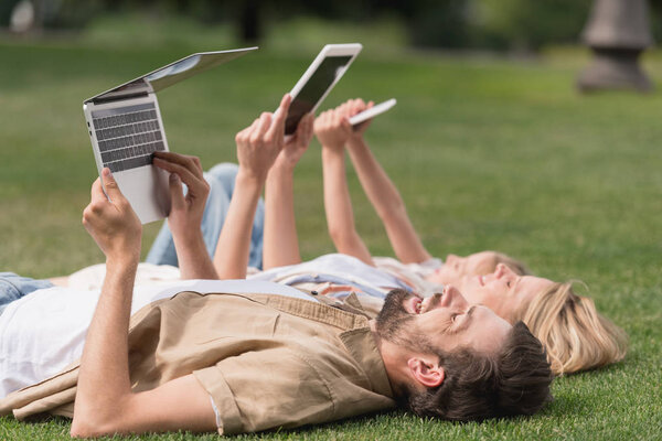 happy family lying on grass and using digital devices