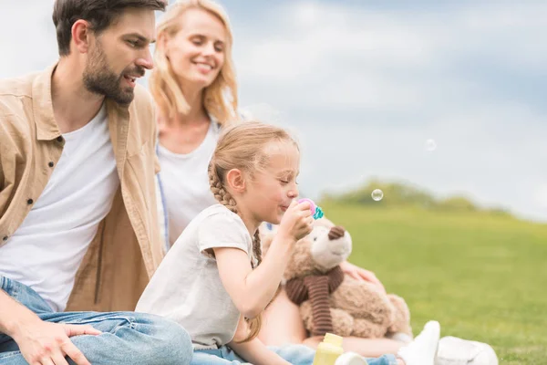 Glückliche Eltern Betrachten Süße Kleine Tochter Mit Teddybär Der Seifenblasen — Stockfoto