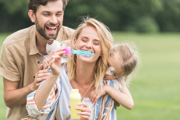 Família Feliz Com Uma Criança Abraçando Soprando Bolhas Sabão Parque — Fotografia de Stock