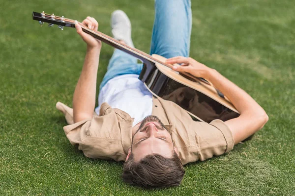 若い男が草の上に横たわるとアコースティック ギターを演奏 — ストック写真