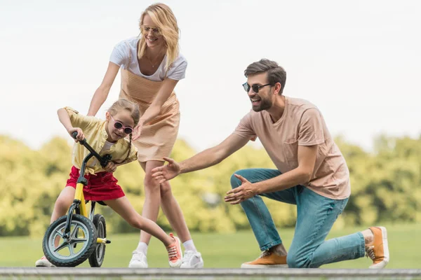 公園でかわいい小さな娘乗って自転車を見て幸せな親 — ストック写真