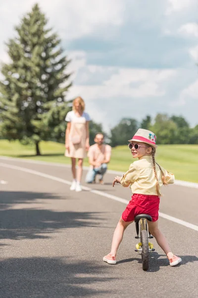 Criança Óculos Sol Andar Bicicleta Enquanto Pais Atrás Parque — Fotografia de Stock