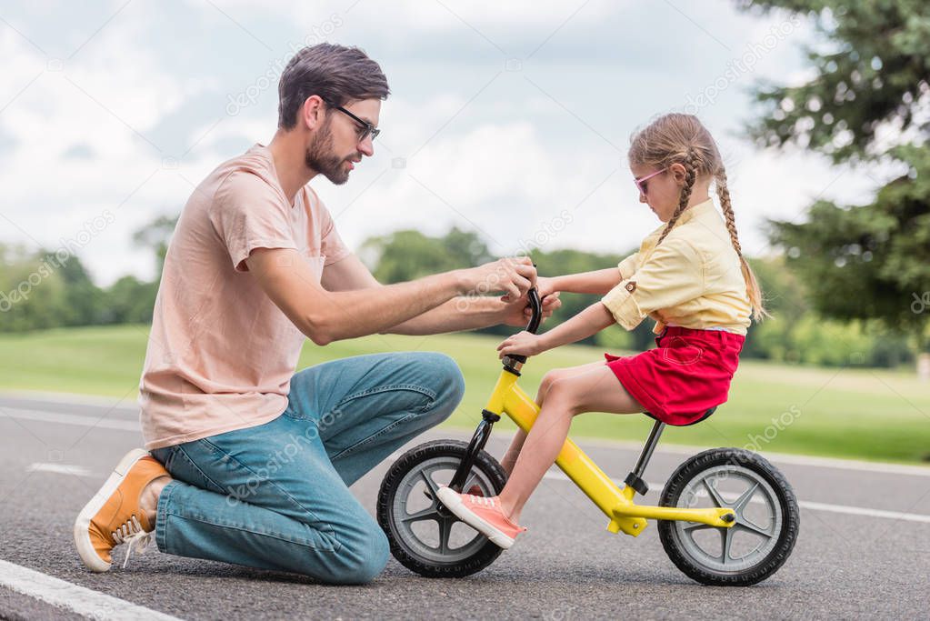 side view of father helping little daughter riding bicycle in park