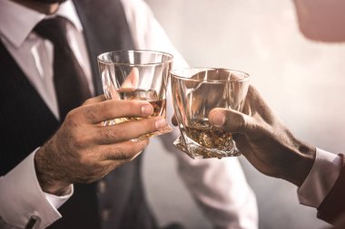 cropped shot of two men in formal wear clinking whiskey glasses